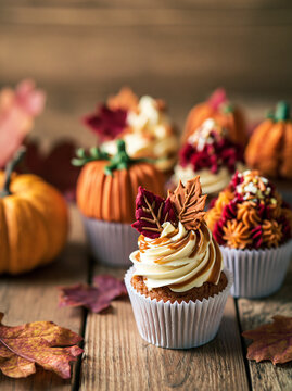 Autumn cupcakes with cream frosting decorated with caramel and sugar maple leaves on rustic wooden table with pumpkins. Thanksgiving and fall seasonal baking. Homemade holiday dessert concept.