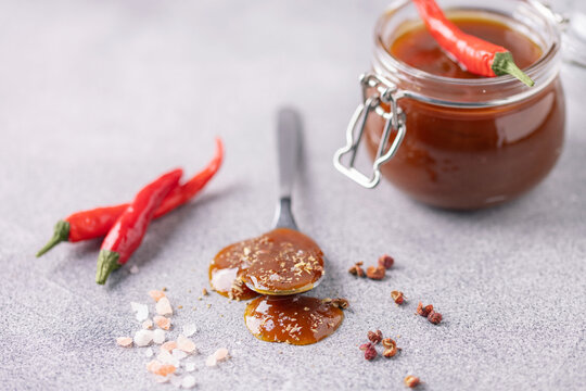 Glass jar with salted caramel with chili pepper on grey background. Trendy swicy food