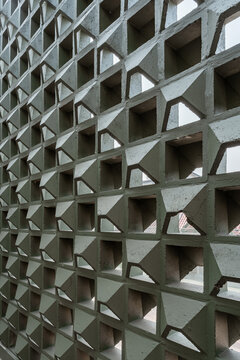 Close up angle shot of an olive green ventilation breeze block wall showcasing 3D geometric pattern cutouts, textured concrete material, and modern architectural facade elements.