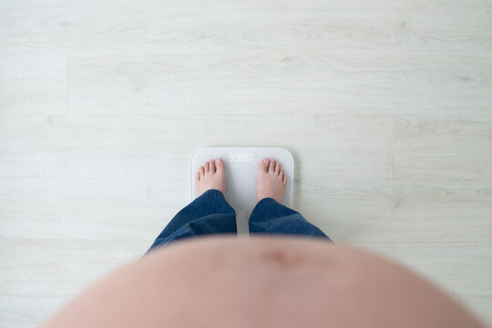 Pregnant woman with big belly standing on weight scale at home. Healthy weight gain during pregnancy avoid pregnancy complications such as gestational diabetes, preeclampsia, and cesarean delivery.