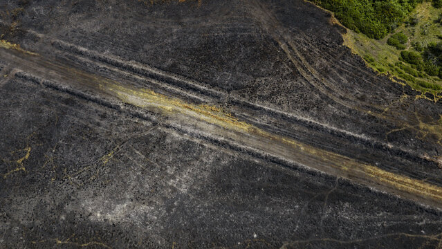 Aerial view of scorched earth and burnt vegetation following a wildfire, with visible tracks cutting through the charred landscape in France.