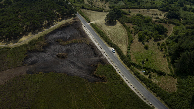 Aerial view of a burnt patch of vegetation next to a road with a car driving through a rural landscape in France.
