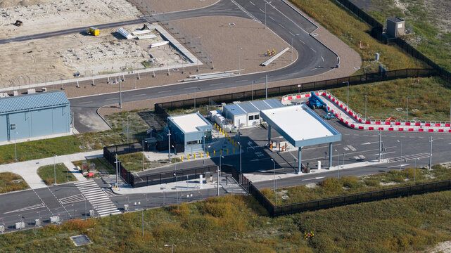 Aerial view of a security checkpoint with a gatehouse and canopy, surrounded by paved roads, fencing, and industrial land in Groningen, Groningen, Netherlands.