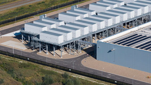 Aerial view of a large industrial data center with rows of cooling units and HVAC systems, surrounded by asphalt roads and green landscape in Groningen, Groningen, Netherlands.