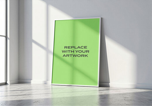 Vertical framed poster mockup leaning against a light gray wall in modern interior with natural from window, placeholder surface, concrete floor, realistic art presentation template
