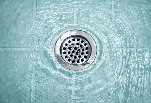 Top view of a chrome shower drain surrounded by clear water ripples on teal tiles, creating a clean, modern bathroom drainage and plumbing scene.