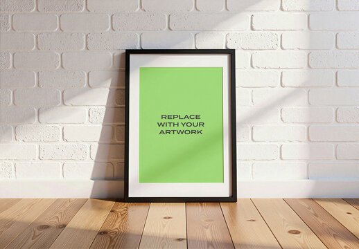 Vertical framed poster mockup with placeholder art displayed on a white brick wall, realistic interior scene wooden floor and natural sunlight, presentation, graphic design template