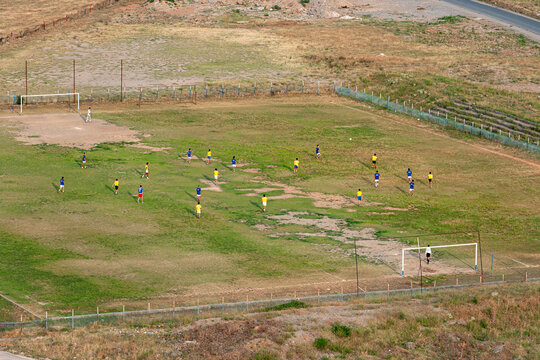 Aerial view of a soccer match with players in blue and yellow jerseys on a grass field in Montenegro.