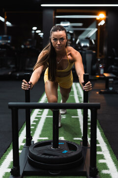 Focused woman pushing weighted sled on gym turf track