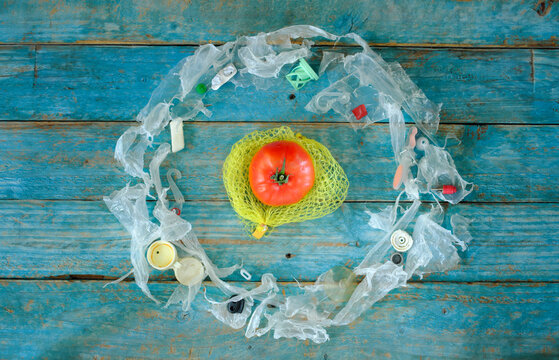 Pollution of vegetables and other food with microplastic, single tomato surrounded by plastic waste, close up shot,free copy space