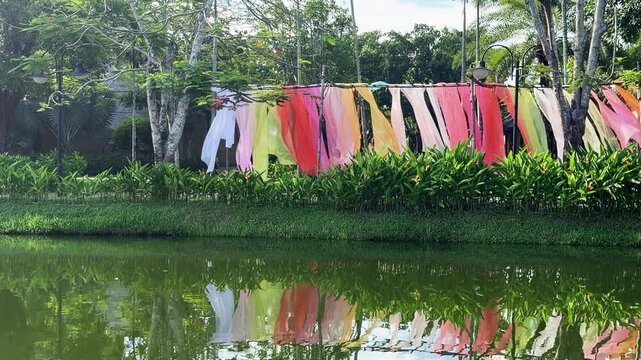 Vibrant outdoor art installation made of translucent pink, orange, yellow, green and white fabrics flowing in wind along landscaped park walkway, shot handheld. High quality 4k footage