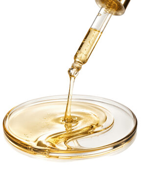 Cosmetic oil dropper dispensing golden serum onto a glass dish isolated on transparent background