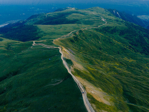 Aerial view of Koruldi Lakes featuring a winding dirt road along the lush green mountain ridge in Mestia, Samegrelo-Zemo Svanet, Georgia.