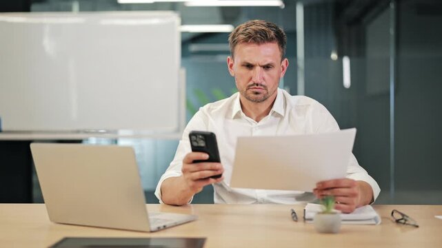 Focused professional compares data on smartphone and documents. Efficient workflow demonstrated within modern office setting. Diligent attention to detail crucial for project success.