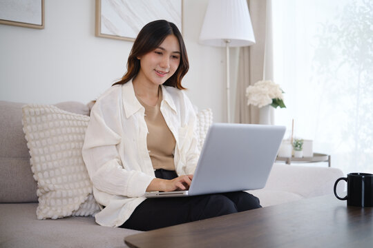 Asian businesswoman working remotely on a laptop with coffee at home.