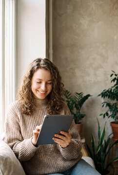 Woman holding tablet smiling by window with green plants