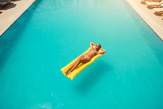 Woman floating on yellow pool float in turquoise swimming pool