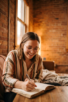 Woman writing in journal by window with golden sunlight streaming through