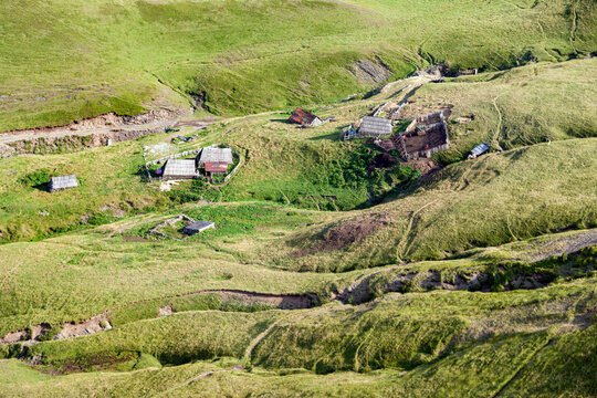 Aerial view of small wooden huts and livestock enclosures nestled in the rolling green hills of the countryside, Montenegro.