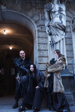Gothic team of three at an old building entrance with atlas statue, dark fantasy group portrait.