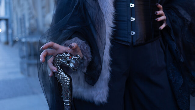 Hand with dark manicure on a silver dragon head walking cane, gothic accessory close up.