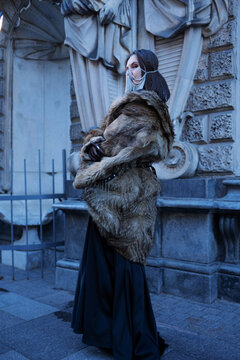 Rear view of woman wrapped in a long fur coat at old facade, luxury winter outerwear look.