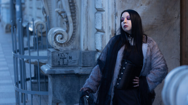 Woman in fur coat and leather corset on an old city street, gothic street style, copy space.