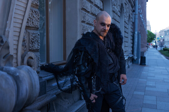 Man in long black coat with fur collar on a city street, male gothic street style, full length.