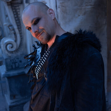 Square format portrait of a man in gothic coat with fur collar, avatar and profile picture.