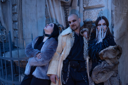 Group of three friends in gothic outfits and fur coats near an old facade, subculture