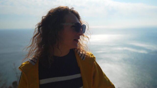 Woman sea overlook young lady in yellow jacket and sunglasses enjoys a beautiful ocean view from a cliffside balcony