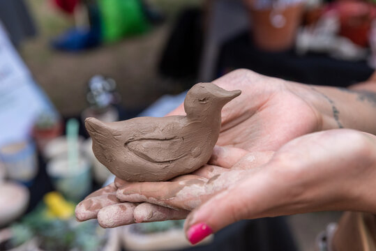 Artisan hands holding a bird or duck sculpture freshly modeled from natural clay