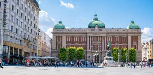 Naklejka premium Belgrade National Museum with green domes and equestrian monument on Republic Square, surrounded by historic buildings, cafes, and visitors