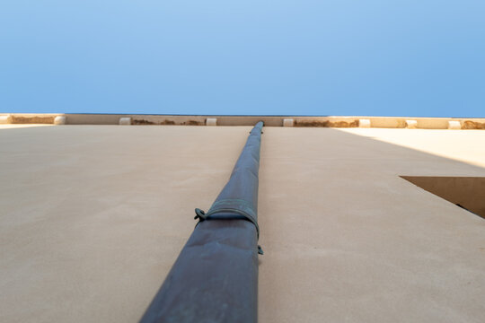 Rustic industrial pipe against textured concrete wall under bright sky