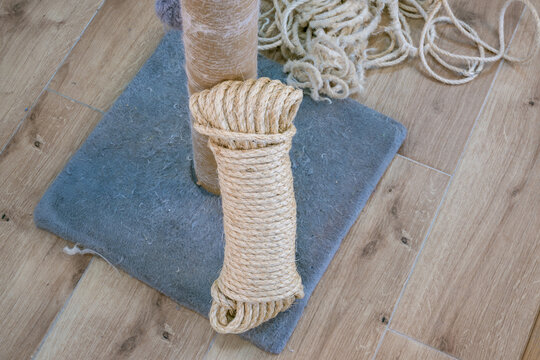 Replacing worn sisal rope on a cylindrical scratching post beside loose cord, with a gray felt base on light wood flooring