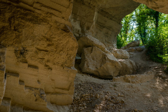 Natural sandstone rock shelter with eroded cave walls, boulders, and leafy forest path at Beli Majdan in Fruska Gora, Serbia