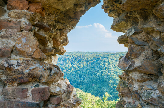 Stone window opening in the ruins of Vrdnicka kula overlooking a green forest and distant horizon under a bright blue sky in Fruska Gora, Serbia