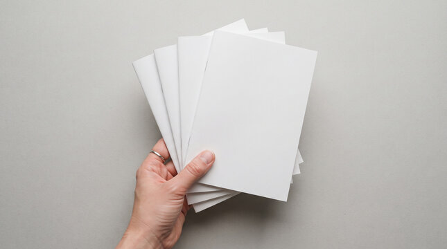 Hand holding a stack of blank white brochures or booklets mockup on a neutral grey background