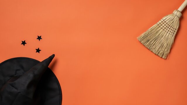 Halloween background with witch hat and broom on orange surface