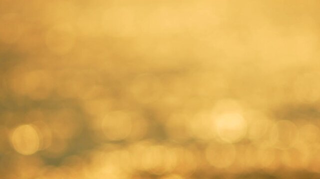 Sunlight reflections shimmer across water surface creating abstract warm orange patterns at sunset. Extreme close-up soft focus shot.