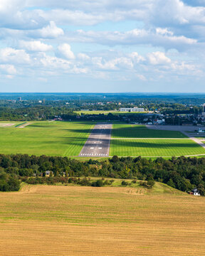 Aerial view of S. Darius and S. Girenas Aerodrome with its paved runway set amidst green fields, surrounding trees, and the city skyline of Kaunas, Kaunas County, Lithuania.