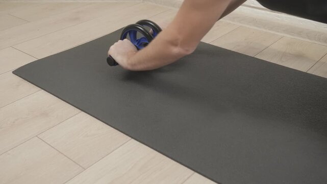 Hands rolling ab wheel forward on black foam mat during home core workout, low diagonal viewpoint with soft diffuse light, with abwheel, exercise, mat, workout detail