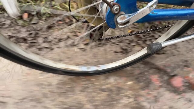 close shot of bicycle wheel hitting water, spinning bicycle rim sprays mud and water everywhere