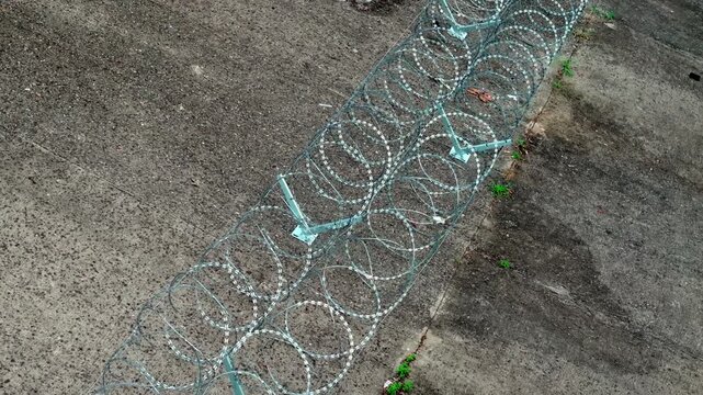 Overhead tracking view of razor wire rows across concrete