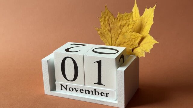 First of November date on white wooden calendar and tiny yellow maple baby leaves as symbols of beginning of the last fall month with terracotta background