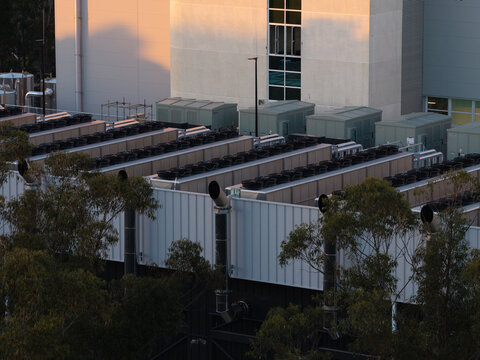 Aerial view of a data center rooftop featuring rows of industrial cooling fans and exhaust pipes set against a modern building facade in Sydney, New South Wales, Australia.