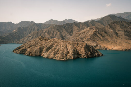 Aerial view of Orto Tokoy Reservoir with turquoise water surrounded by arid, rugged mountain ranges under a clear sky in Kyrgyzstan.