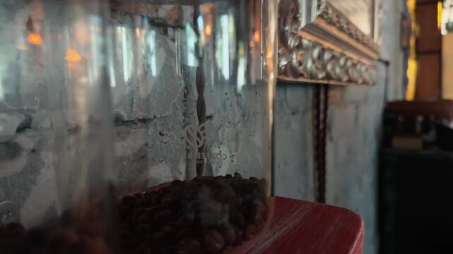 Handheld Close Up Dolly Tracking Shot Sliding Along Rows of Whole Dark Roasted Coffee Beans Stored in Glass Jars on Weathered Scratched Wooden Shelf inside Rustic Loft Cafe with Concrete Wall