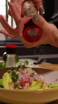 Vertical video. Female Hands Grind Black Pepper over Bowl of Fresh Avocado, Tomato, Onion and Cilantro, Seasoning Homemade Guacamole