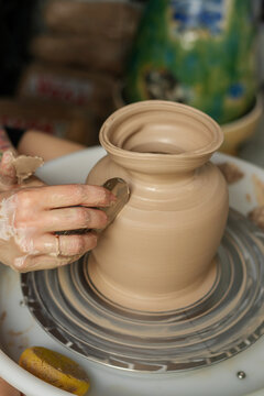 Potter shaping a clay pot on a spinning wheel. Hands covered in mud. 